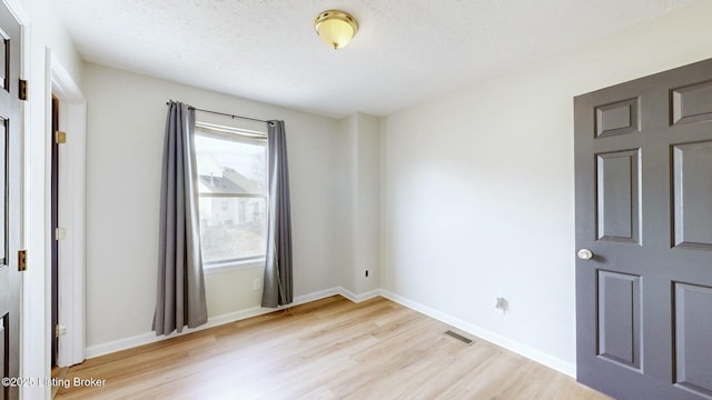 spare room with light wood-style flooring, visible vents, baseboards, and a textured ceiling