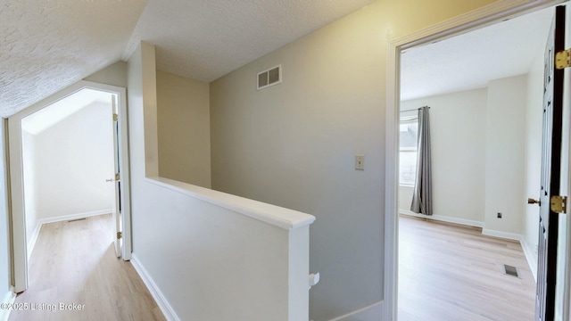 corridor featuring an upstairs landing, visible vents, a textured ceiling, and light wood-type flooring