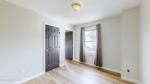 spare room with a textured ceiling, baseboards, and light wood-style floors