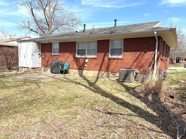 rear view of property featuring brick siding, central AC unit, a lawn, and an outbuilding