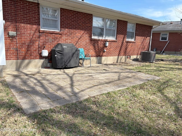 rear view of property with a yard, a patio area, brick siding, and central AC