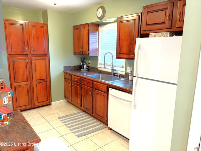 kitchen featuring a sink, dark countertops, white appliances, brown cabinetry, and light tile patterned floors