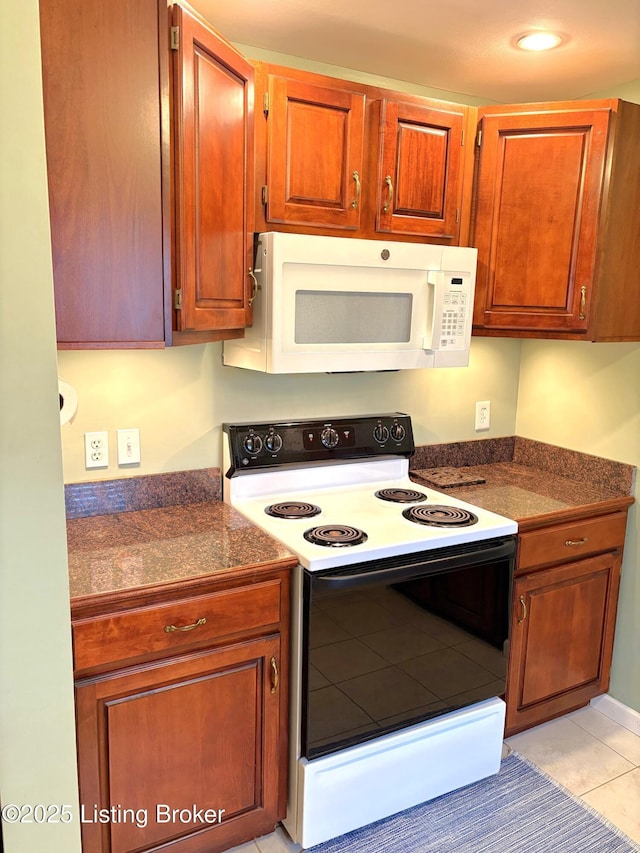 kitchen featuring white microwave, electric range, brown cabinetry, and dark countertops