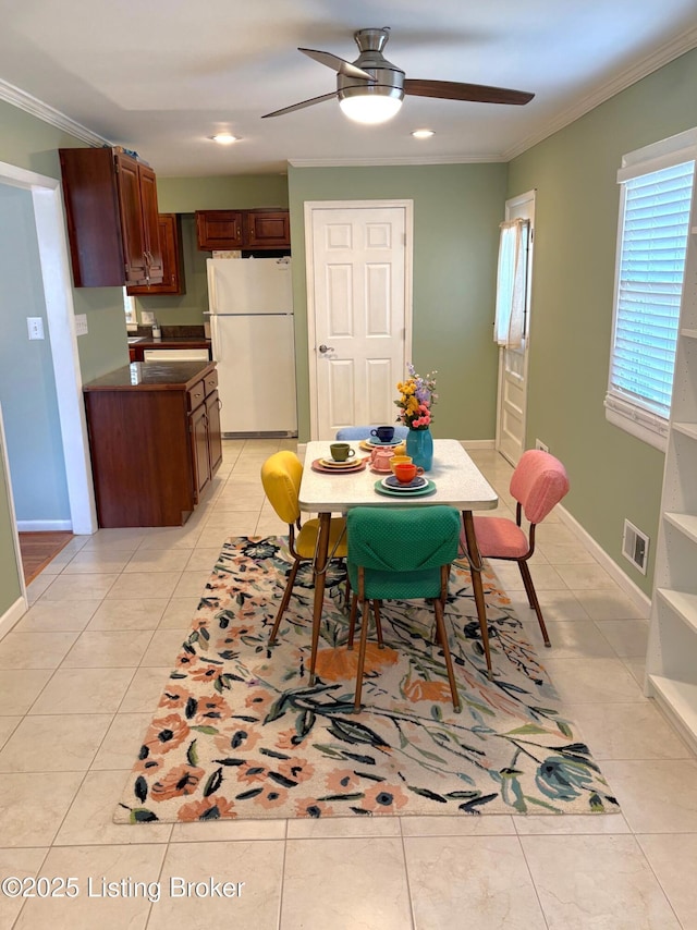 dining room with light tile patterned floors, visible vents, crown molding, and ceiling fan