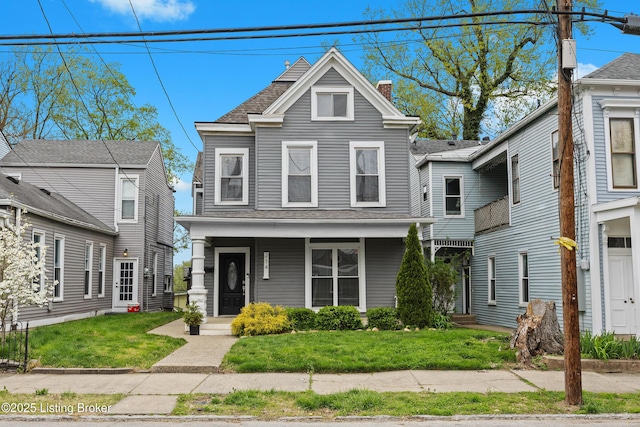 view of front facade featuring roof with shingles, a chimney, a front lawn, and covered porch