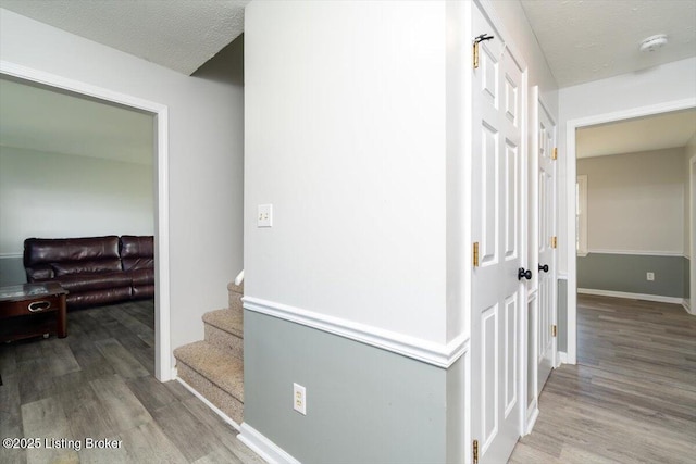 corridor with stairway, a textured ceiling, baseboards, and wood finished floors