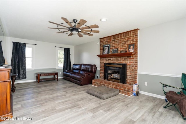 living room with baseboards, a brick fireplace, ceiling fan, and light wood finished floors