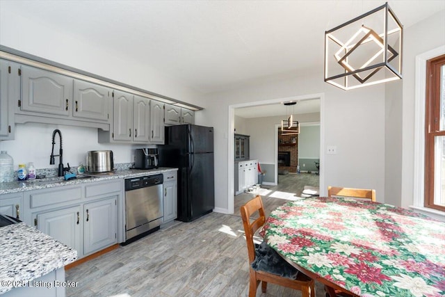 kitchen featuring gray cabinetry, a sink, stainless steel dishwasher, freestanding refrigerator, and light wood finished floors