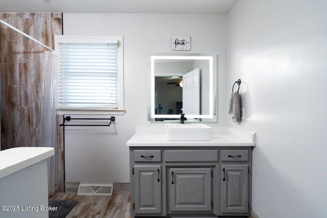 full bathroom with vanity, wood finished floors, visible vents, a tile shower, and ceiling fan