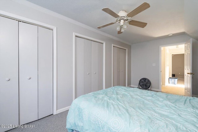 bedroom with multiple closets, a ceiling fan, a textured ceiling, carpet floors, and baseboards