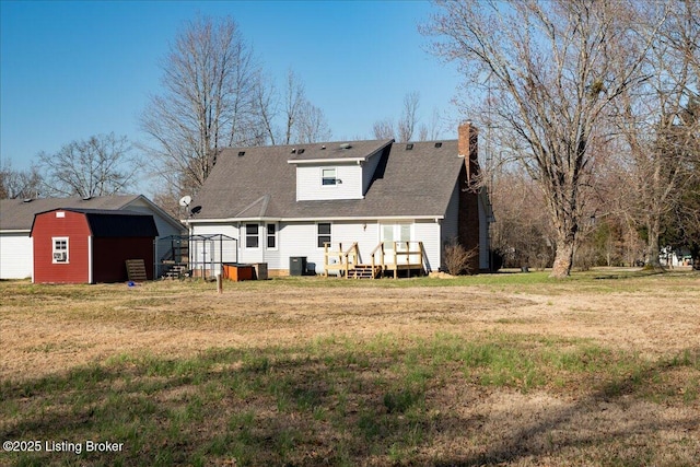 back of property with an outbuilding, central AC unit, a wooden deck, a chimney, and a lawn