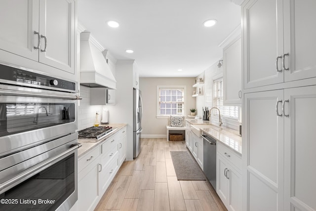 kitchen featuring a sink, decorative backsplash, stainless steel appliances, custom range hood, and white cabinets