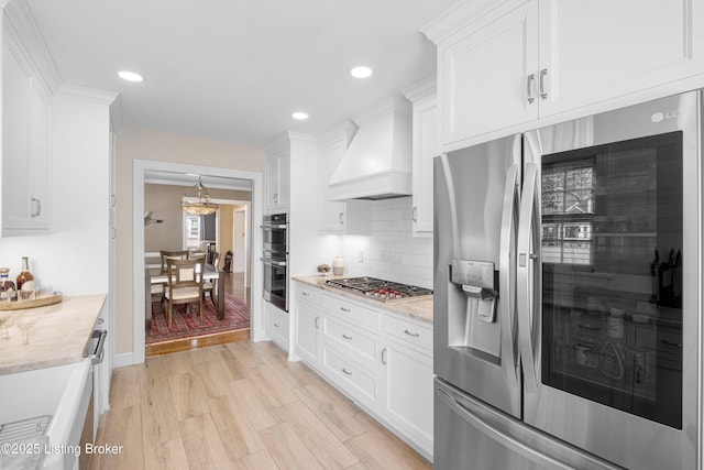 kitchen featuring premium range hood, light wood-style flooring, stainless steel appliances, white cabinets, and decorative backsplash