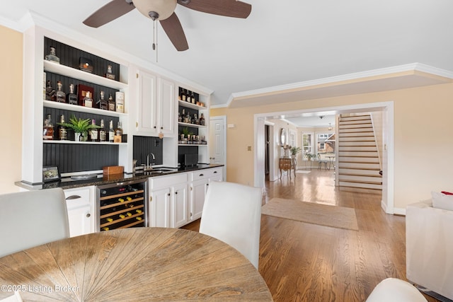 bar featuring a sink, wine cooler, crown molding, indoor wet bar, and stairs