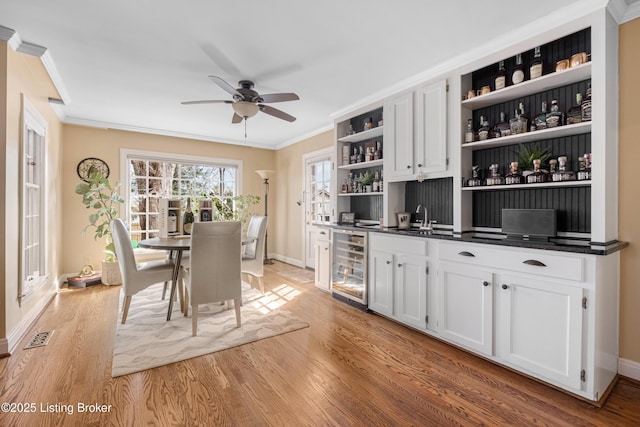 dining area with visible vents, crown molding, wine cooler, indoor wet bar, and light wood-style floors