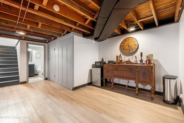 finished basement with a sink, stairway, baseboards, and light wood finished floors