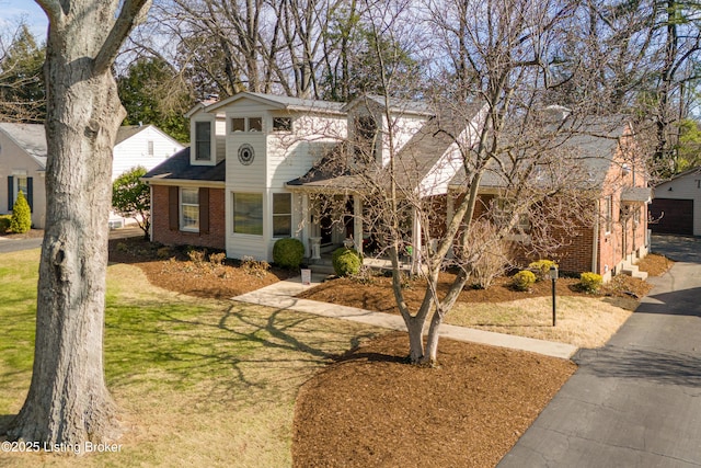 view of front of house featuring a detached garage, brick siding, and a front lawn