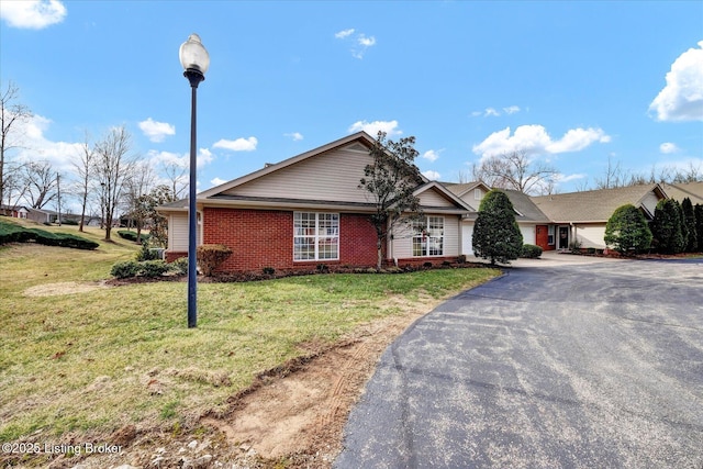 single story home featuring brick siding, aphalt driveway, and a front yard