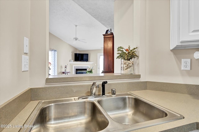 kitchen featuring a sink, a healthy amount of sunlight, a fireplace, and white cabinetry