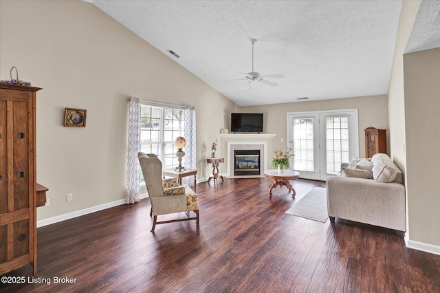 living area with a ceiling fan, baseboards, dark wood finished floors, a textured ceiling, and a tiled fireplace