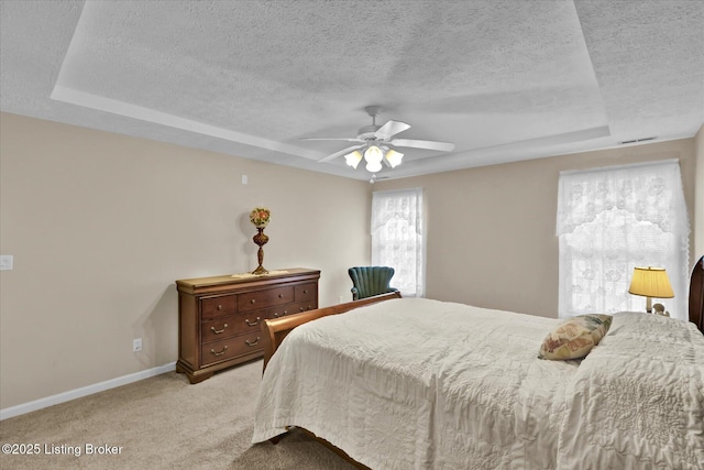 bedroom featuring baseboards, light colored carpet, a raised ceiling, and a textured ceiling