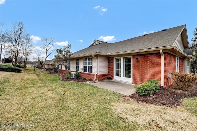 back of property with a patio area, a lawn, brick siding, and roof with shingles