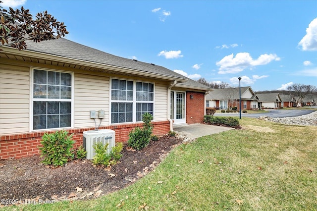 back of property featuring brick siding, central air condition unit, a lawn, and a shingled roof