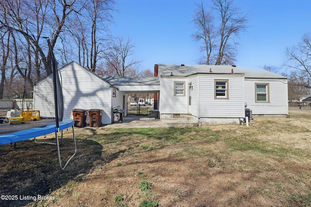 back of property with an attached carport, a trampoline, a yard, crawl space, and a patio