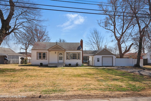 view of front facade featuring driveway, a chimney, a front yard, and fence