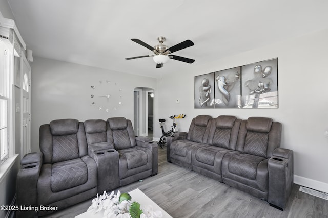 living room featuring a ceiling fan, visible vents, wood finished floors, baseboards, and arched walkways