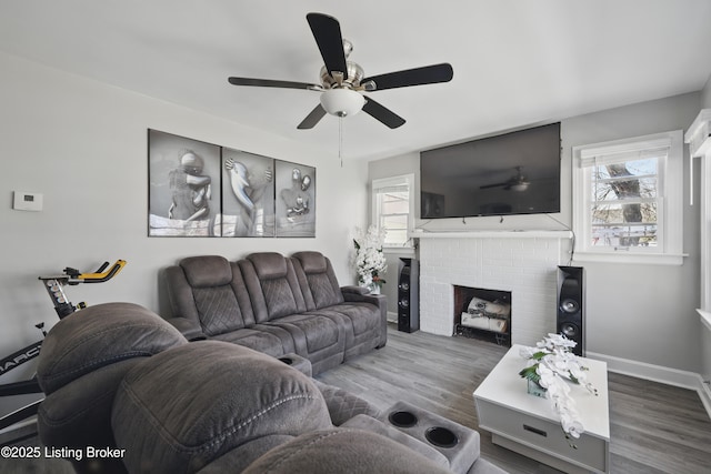 living area with a ceiling fan, a brick fireplace, wood finished floors, and baseboards