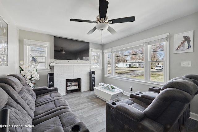 living area featuring a brick fireplace, a ceiling fan, light wood-type flooring, and baseboards