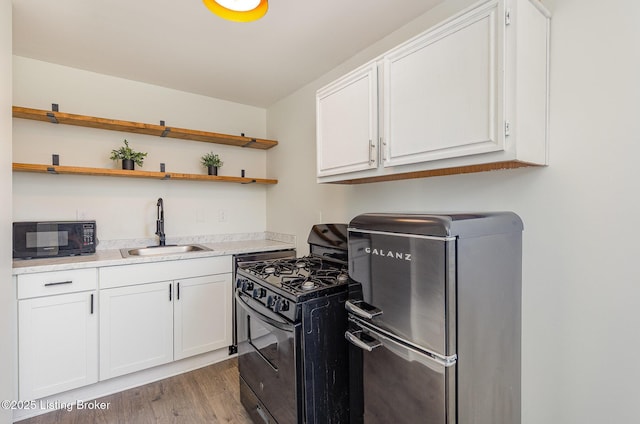 kitchen featuring black appliances, a sink, white cabinetry, light wood finished floors, and light countertops