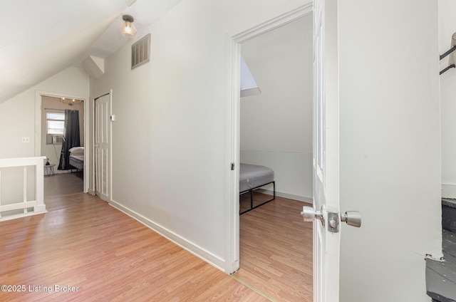 hallway featuring vaulted ceiling, baseboards, visible vents, and light wood finished floors