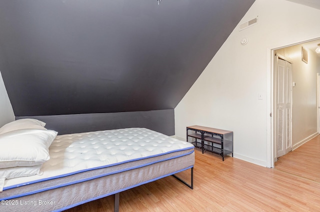 bedroom with visible vents, wood finished floors, baseboards, and vaulted ceiling