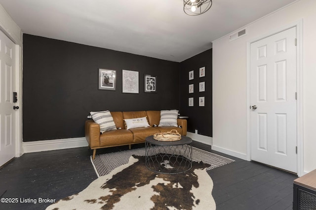 living area with an accent wall, baseboards, visible vents, and dark wood-style flooring