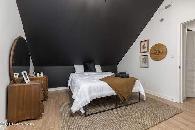 bedroom with visible vents, baseboards, light wood-style floors, and lofted ceiling