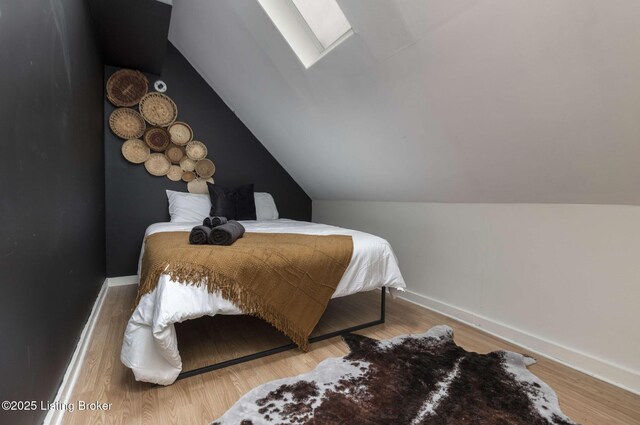 bedroom featuring lofted ceiling with skylight, baseboards, and wood finished floors