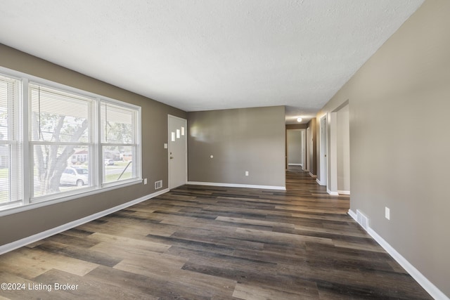 empty room featuring visible vents, baseboards, a textured ceiling, and dark wood-style floors