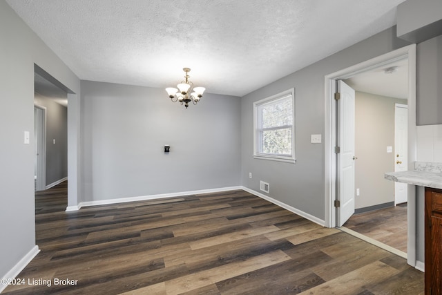 unfurnished dining area with baseboards, a textured ceiling, an inviting chandelier, and dark wood-style floors