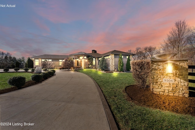 prairie-style house featuring a front yard, stone siding, driveway, and a chimney