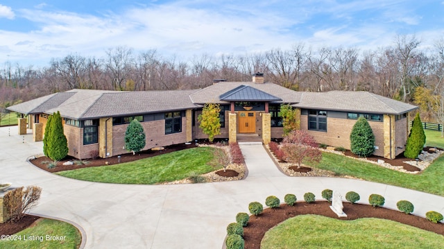 view of front of house with concrete driveway, a front yard, a shingled roof, brick siding, and a chimney