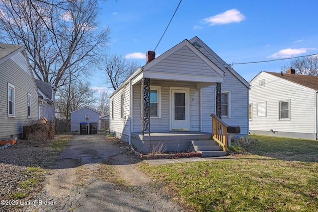 shotgun-style home featuring aphalt driveway, a porch, a chimney, and a front yard