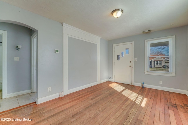 foyer entrance featuring visible vents, light wood-style floors, arched walkways, and baseboards