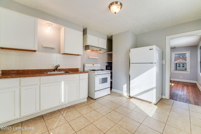 kitchen with dark countertops, light tile patterned flooring, white appliances, white cabinetry, and a sink