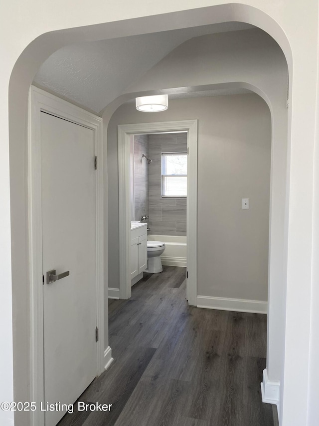 hallway with baseboards, lofted ceiling, and dark wood-style flooring