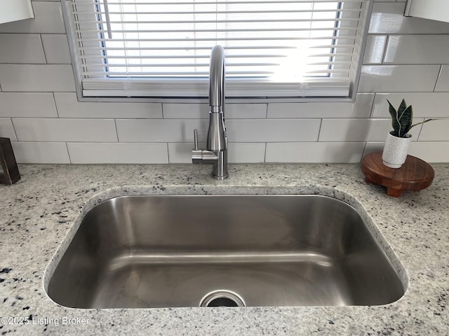 room details with decorative backsplash, light stone counters, and a sink