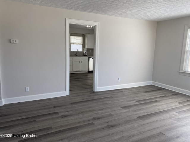 spare room featuring a sink, dark wood-style floors, baseboards, and a textured ceiling