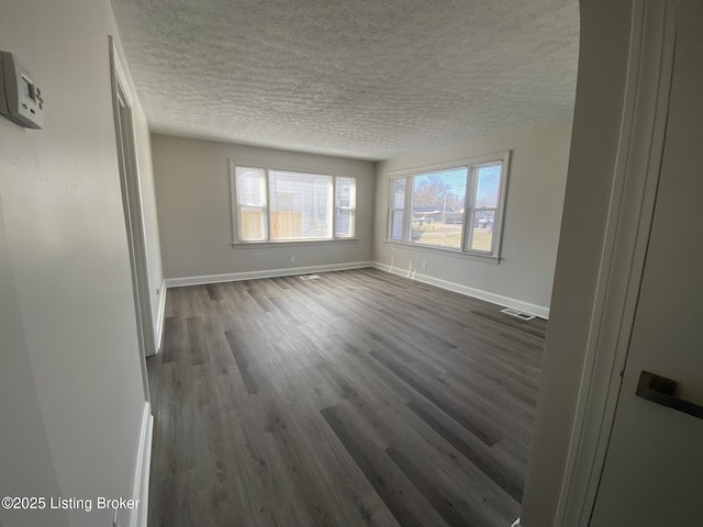 unfurnished room with dark wood finished floors, visible vents, baseboards, and a textured ceiling