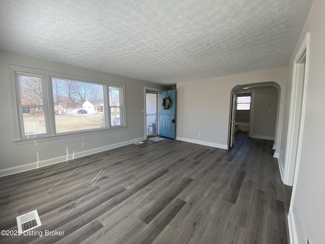 unfurnished living room featuring visible vents, a textured ceiling, arched walkways, baseboards, and dark wood-style flooring